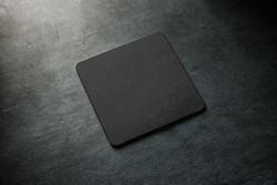 Blank black beer coaster mockup lying on grey desk. Square clear dark bar cork table-mat design mock up top side view. Quadrate cup or bottle rug display, isolated.