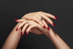 Beautiful glamour photo of elegant female hands with bright burgundy manicure on gray background. Long square nails with dark red gel polish. Luxury fashion style of brilliants jewelry rings