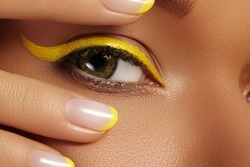 Beautiful macro close-up of female Eye with bright yellow Eyeliner Makeup. Neon Disco make-up and Fashion Manicure. Summer beauty styleCloseup macro shot of fashion liner eyes visage