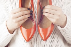 Fashion studio shot of shopping girl holding a red  high heel shoe in her hand on a light background.