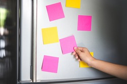 hand holding blank sticky paper note on refrigerator door
