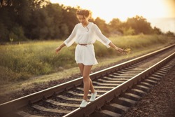 Girl balancing on train rail. Attractive young woman walking outdoors