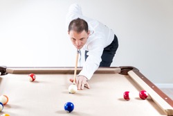 Young man, businessman in tie and white shirt holding cue by pool table, playing game of billiard by striking white ball