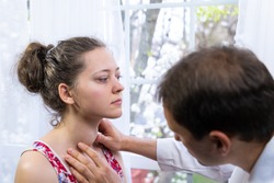 Doctor inspecting, doing palpation examination of young woman with Grave's disease hyperthyroidism symptoms of enlarged thyroid gland goiter and ophthalmopathy in hospital