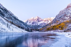 Maroon Bells morning sunrise reflection with sunlight on peak in Aspen, Colorado rocky mountain and autumn yellow foliage view and winter snow frozen lake