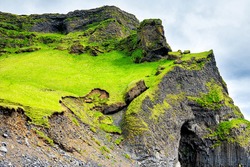 Icelandic green meadow field grass hill mountain rocky cliff landscape in Iceland summer in Reynisfjara, Vik with basalt cave