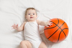 5 month old baby lying on his back on white sheet playing basketball