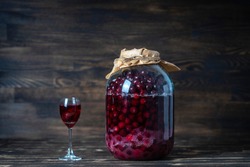 Homemade tincture of red cherry. Berry alcoholic drinks concept. Homemade red wine made from ripe cherries in a large glass jar and a wineglass on wooden background, Ukraine