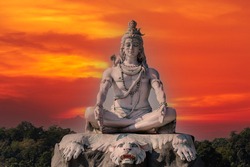 Statue of meditating Hindu god Shiva against the red sky on the Ganges River at Rishikesh village in India, close up
