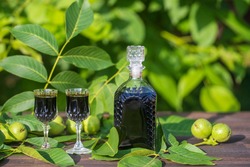 Liqueur from young green walnuts, remedy for stomach ache, close up. Tincture of green walnuts in a glass bottle on a table in the garden