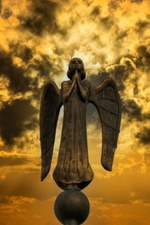 Detail of beautiful bronze statue of an angel with wings against the dark sky with clouds. Beautiful angel with a stormy sky background , close up