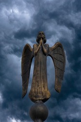 Detail of beautiful bronze statue of an angel with wings against the dark sky with clouds. Beautiful angel with a stormy sky background , close up