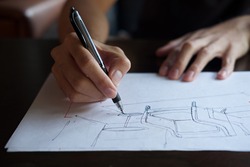 The hand of the designer with a pen, designing and sketching a furniture product