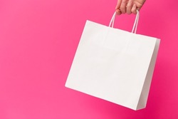 Female hand holding white blank shopping bag isolated on pink background. Black friday sale, discount, recycling, shopping and ecology concept