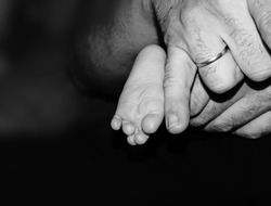            foot of a newborn baby with father's hand (little finger).
 Small foot (leg) of a small baby. child with dad black and white photo, background                    