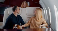 Happy wealthy family with preteen daughter and cocker spaniel dog flying together on private jet. Mature elegant man and woman relaxing in leather chair with little daughter jumping in first class