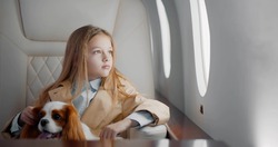 Portrait of cute preteen girl travelling with cocker spaniel dog by commercial airplane. Adorable child with pet sitting in first class jet flying alone