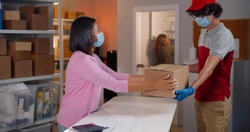Courier in safety mask deliver parcel to woman in workshop. Online store warehouse manager wearing protective mask receive return order from deliveryman