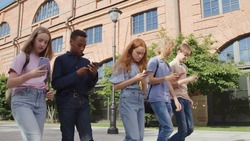 Group of multinational college students obsessed with smartphones walking outdoors. Multiethnic teens use cellphone walking together after school
