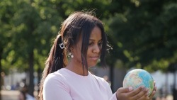 African-American teenage girl holding globe of earth standing in park. Environment and ecology concept