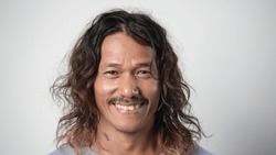 40s asian man with long curly hair look camera thailand. Happy adult thai guy portrait. One 30 year old cute korean person smile. Chinese male head shot. Japanese face close up. Vietnamese people asia