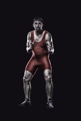 Freestyle wrestler in red uniform in ready position isolated on black background