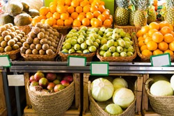 fresh vegetables and fruits in wicker baskets on counter of greengrocery