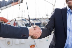 handshake of two businessmen near the yachts in the port