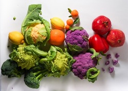 Group of fresh vegetables and fruit in rainbow composition on light background. Appetite vegan ingredients with cauliflower, Romanesco, pomegranate, lemon, mandarin, broccoli, orange and red paprika