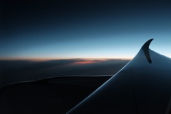 Beautiful sky clouds seeing through the Airbus A350 windows. Sunset aerial view through airplane window over wings. Flying at sunset and looking out of the window and enjoying the panoramic view.