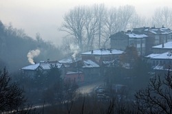 Blurry view of the empty street, houses with smoking chimneys, trees and heavy fog in Bulgaria