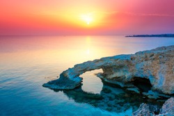 Beautiful Arch in the rocks by the sea in Ayia Napa. The bridge of lovers on the background of a bright sunny pink sunset. Travel to Cyprus tourism sightseeing islands.