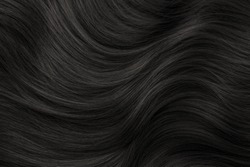 Brunette or brown hair. Female long dark hair in black. Beautifully laid curls. Closeup texture in a dark key. Hairdressing, hair care and coloring. Shading gray hair. Background with copy space.