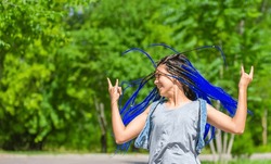 A girl with dreadlocks smiles while walking in the park. A woman with a creative hairstyle has fun in nature.