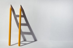 Two pencils and a shadow in form of ladder. Success, teamwork and solving problems business concept. Copy space for text .