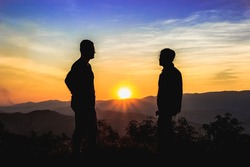 Front view of full body of two men silhouettes, who are looking each other on the mountain with beautiful sky and sunrise