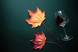 Wine glass with red wine and autumn grape leaves on black background. Creative wine degustation layout in rustic style, selective focus. Flat lay backdrop with copy space, top view.