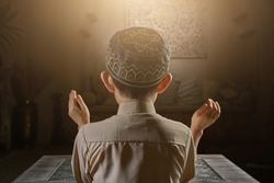 Muslim boy in prayer cap and arabic clothes with rosary beads and holy Koran book praying to Allah, ramadan kareem concept young kid spiritual peaceful moment inside eastern traditional interior
