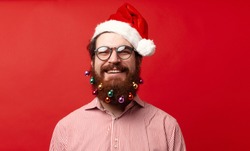 Portrait of cheerful bearded man with decorated christmas beard and wearing santa claus hat