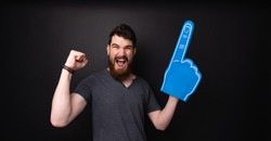 Photo of handsome bearded guy with big fan glove, screaming  and celebrating over  dark background 