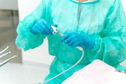 No face photo of a dentist using some dentistry tools for the patient while wearing disposable clothes and gloves.