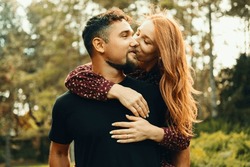 Young cheerful woman kisses her handsome man while staying at his back embracing him.