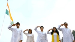 Happy young teenagers saluting Indian national flag - Independence Republic Day. Group of Indian friends in traditional clothing celebrating 26 January or 15 August together in a park - festive scene