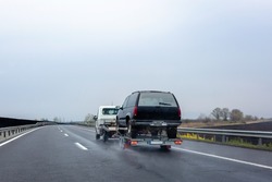 Car carrier trailer with car on wet road. Spray from under the wheels of car