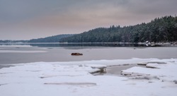 Ice floe at the beach with forest in the background on the other side of the lake