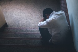 Depressed man sitting head in hands on the stairs in building. with low light environment, dramatic concept, concept of Major depressive disorder, unemployed, sadness, depressed and human problems,