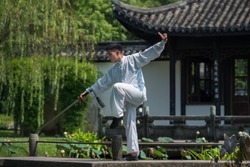 Asian man working out with Tai Chi sword in the morning at the park, Chinese martial arts, healthy care for life concept.