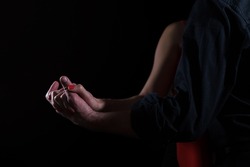Illuminated male and female hands entwined against black background; a young couple - a woman in red and a man in black shirt - dancing tango in the dark; the female hand has red nails.