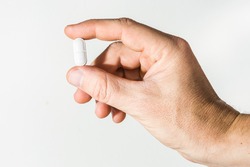 male hand holding a pill against white background