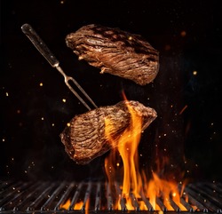 Flying beef steaks over flaming grill grid, isolated on black background. Barbecue and cooking